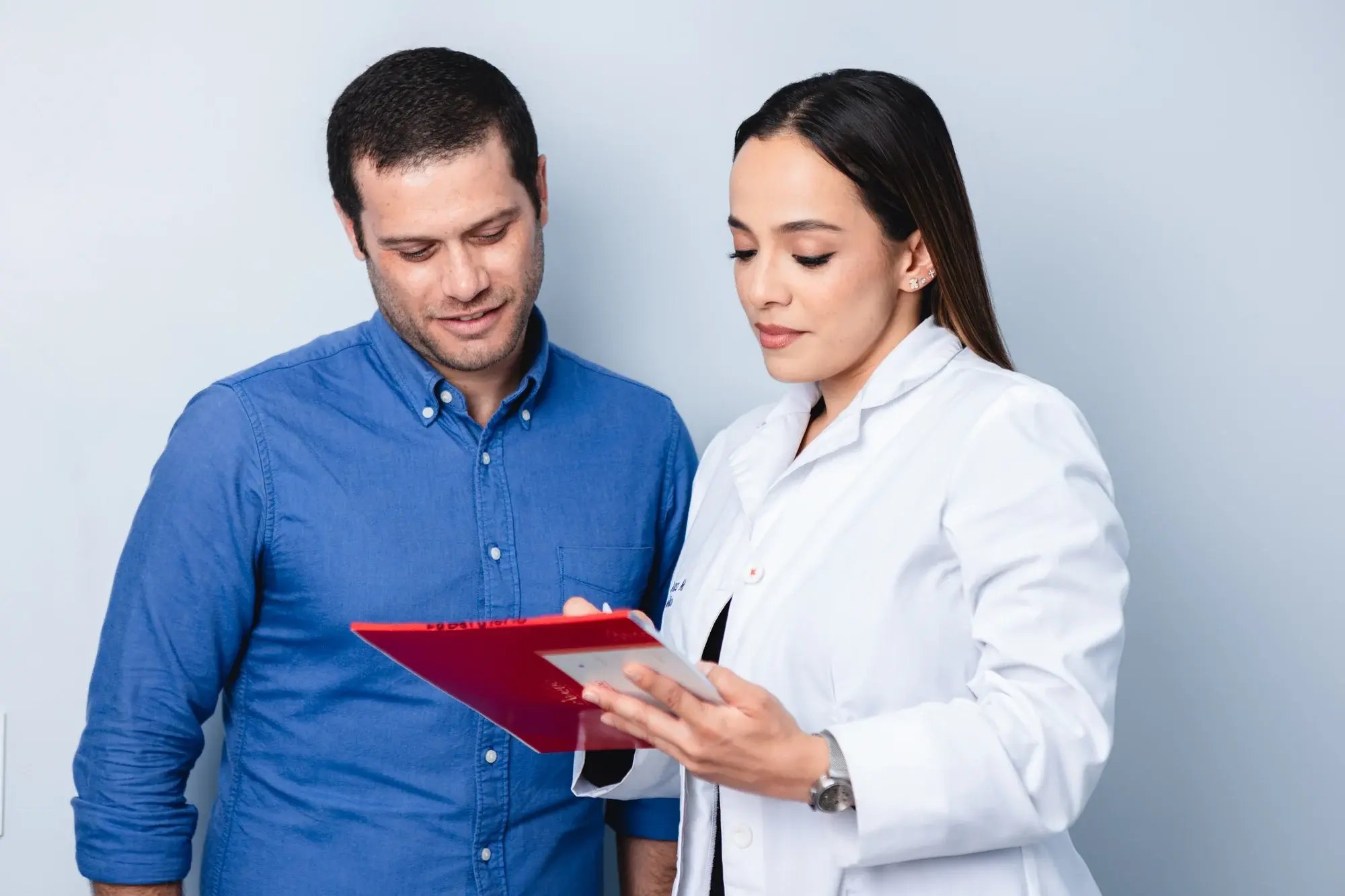 Doctora mostrando resultados médicos en carpeta roja a un paciente.
