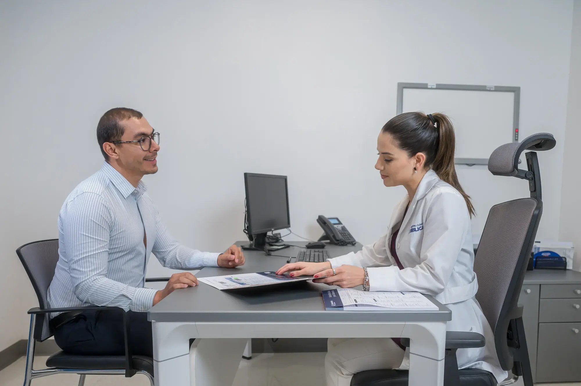 Consulta médica entre paciente y doctora en un escritorio con documentos.