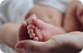 Pie pequeño de bebé sostenido suavemente por una mano.