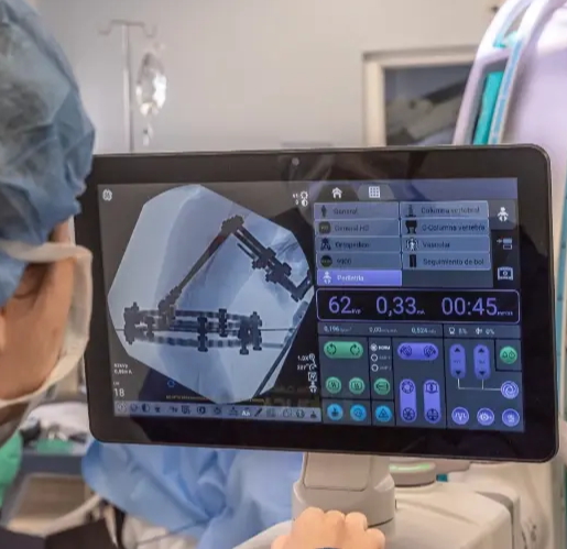 Profesional médico observando una pantalla con imagen tridimensional de columna vertebral durante procedimiento quirúrgico.