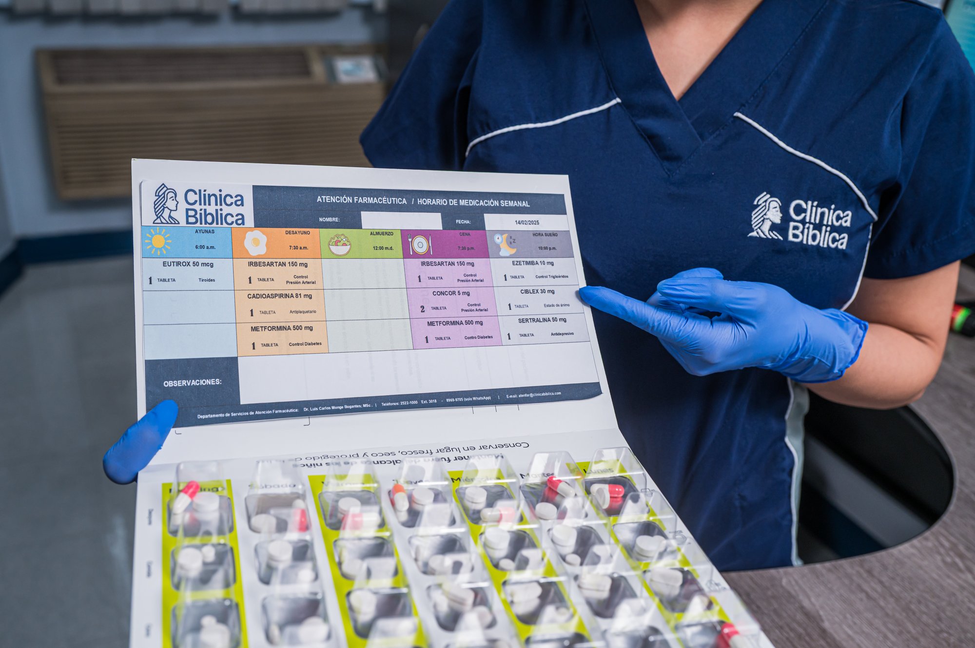 Health professional with blue gloves showing a weekly medication plan next to an organized blister pack with pills at Clínica Bíblica.