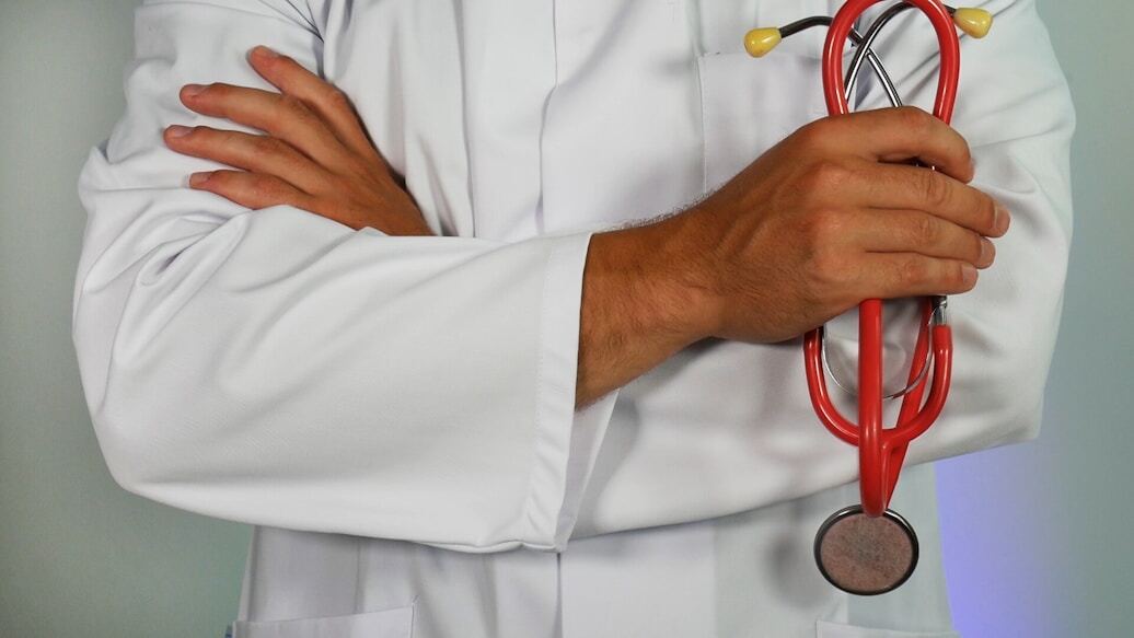 Médico con bata blanca sosteniendo un estetoscopio rojo.