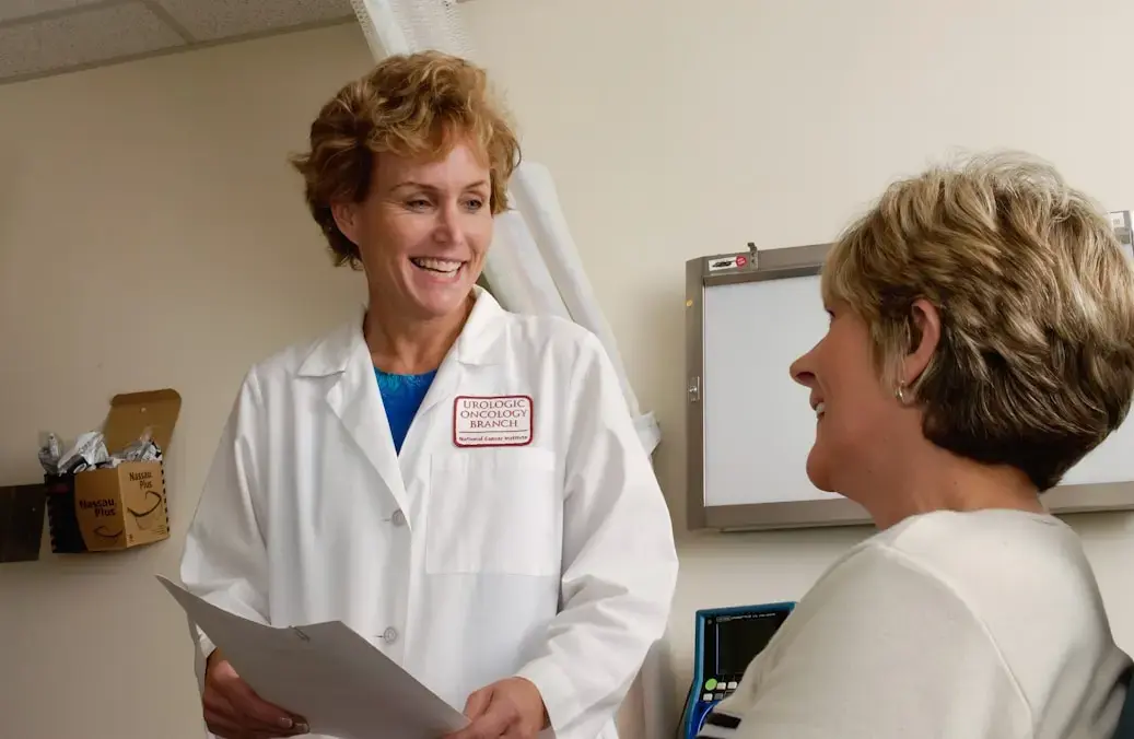Doctora con bata blanca sonriendo mientras conversa con una paciente.