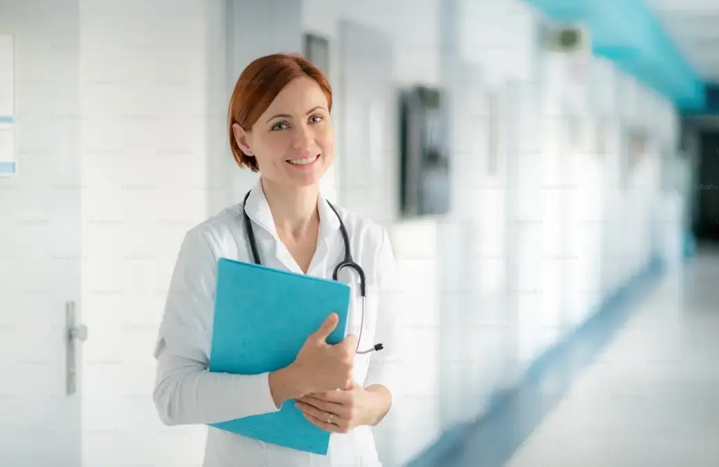 Doctora con estetoscopio sosteniendo carpeta azul en pasillo de hospital.