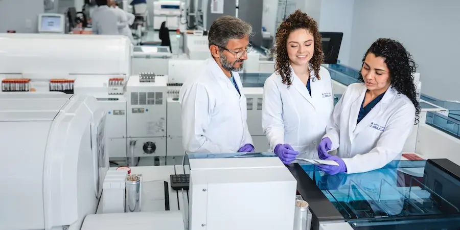 Profesionales de laboratorio clínico de la Clínica Bíblica revisando muestras con tecnología avanzada