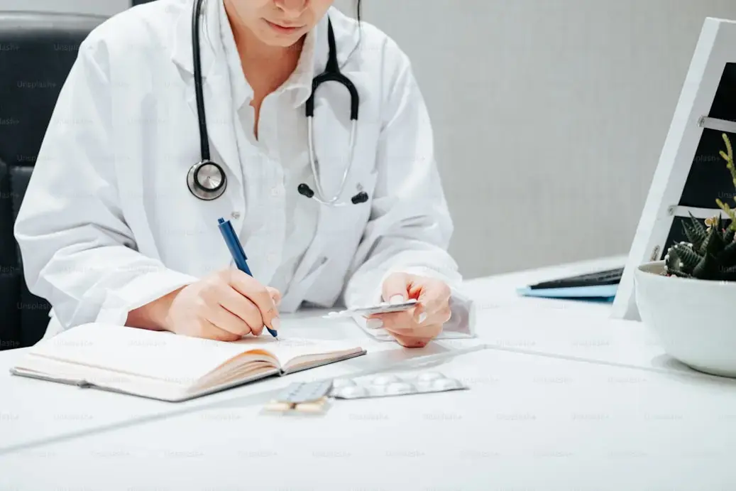 Médico escribiendo receta médica con pastillas sobre el escritorio.