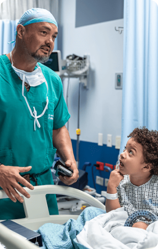Cirujano conversando con un niño paciente en una habitación de hospital antes de una intervención médica.