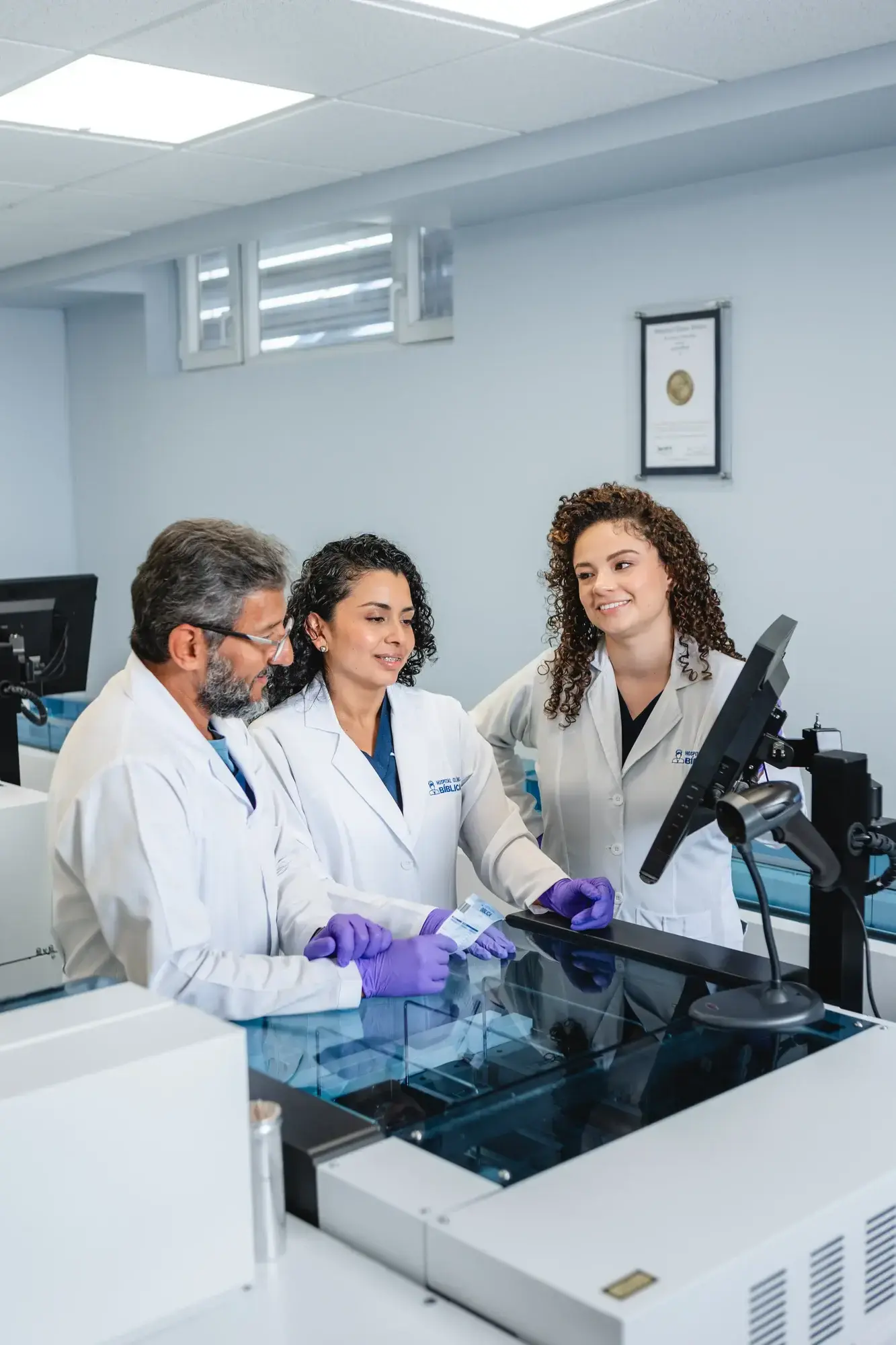 Tres médicos en laboratorio con bata blanca revisando muestras en un monitor
